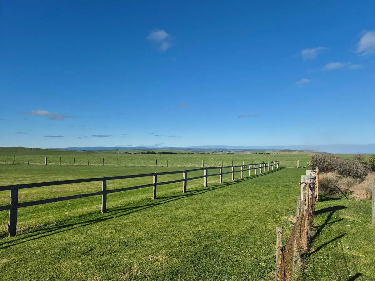 Long post-and-rail fence across open grassland under blue sky