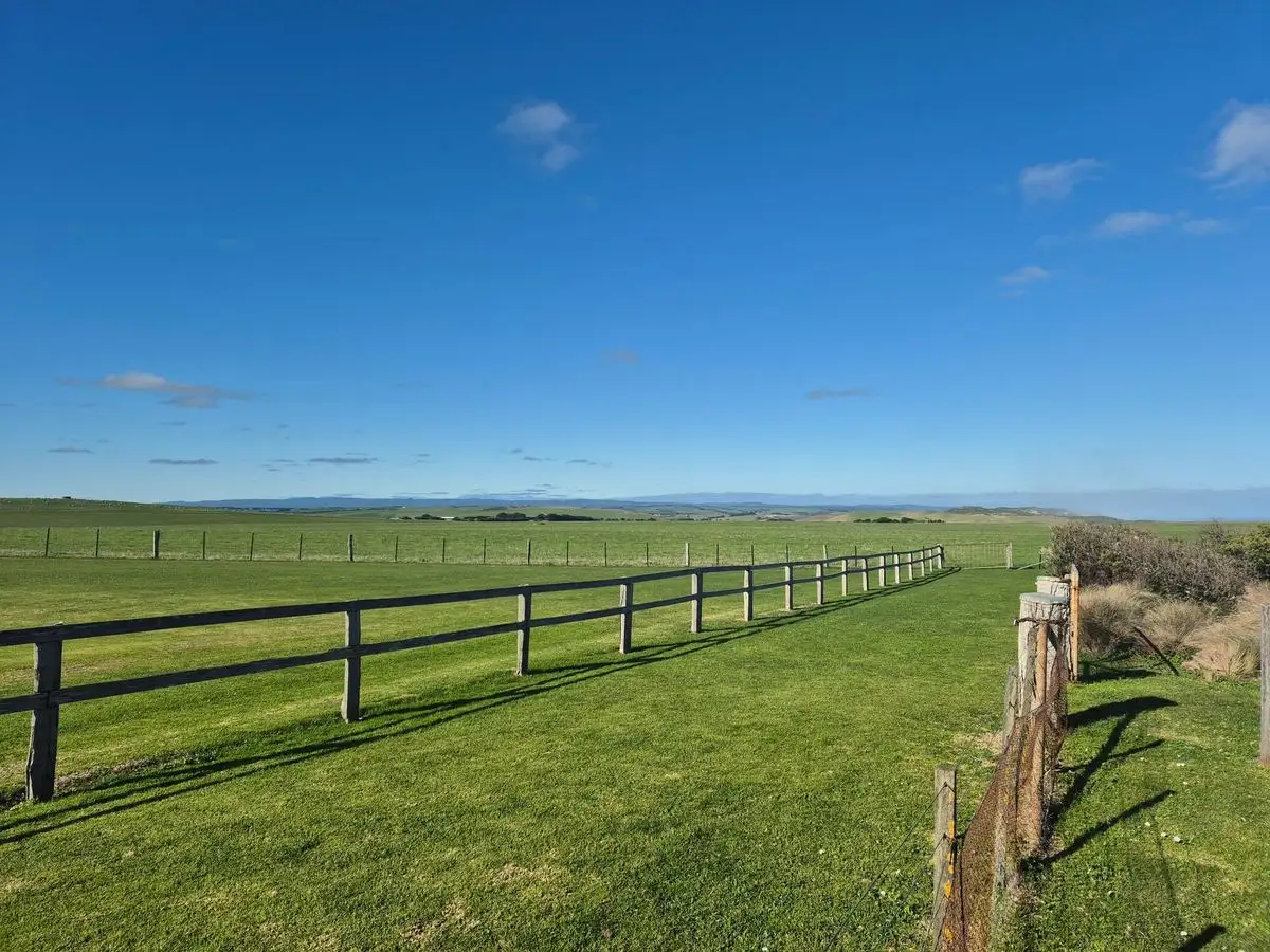 Long post-and-rail fence across open grassland under blue sky